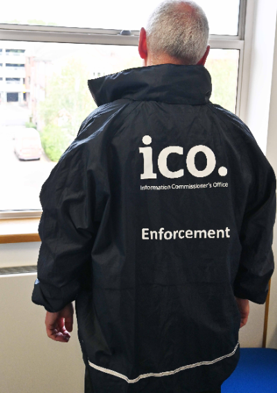 A man looks out of the window. He's wearing a dark blue ICO enforcement jacket.