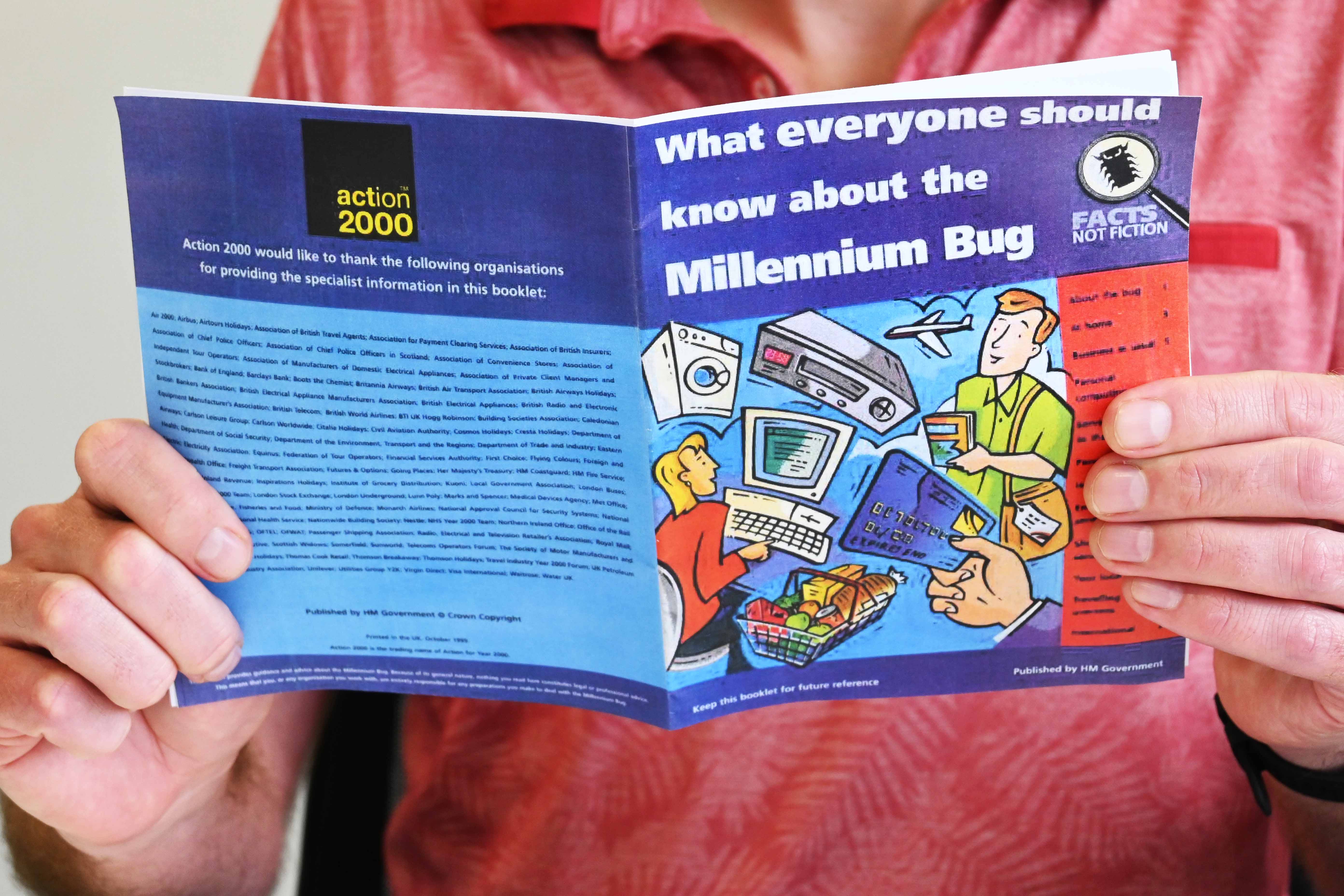  A man is holding and reading a small pamphlet about the Millennium Bug. The pamphlet has series of cartoons on the front representing shopping, flying, using technology like washing machines and computers, using credit cards and shopping. The title reads what everyone should know about the Millennium bug.