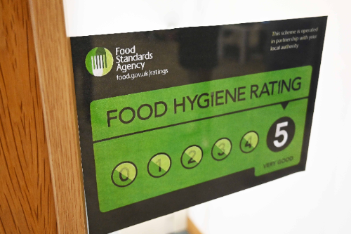 A Food Standards Agency food hygiene rating poster. The black and green poster is stuck up in a doorway. This particular establishment has a five star food hygiene rating.