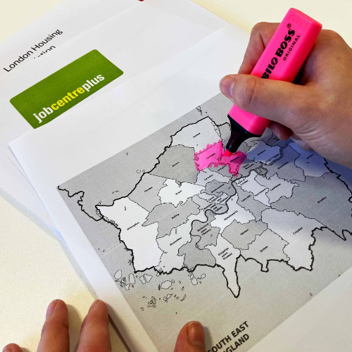 A man is working on a bundle of documents. He's highlighting a map of London. He's already highlighted the areas of Haringey and Hackney. Underneath the map you can see two more document piles. One set is from a London housing association and the other documents from a job centre.