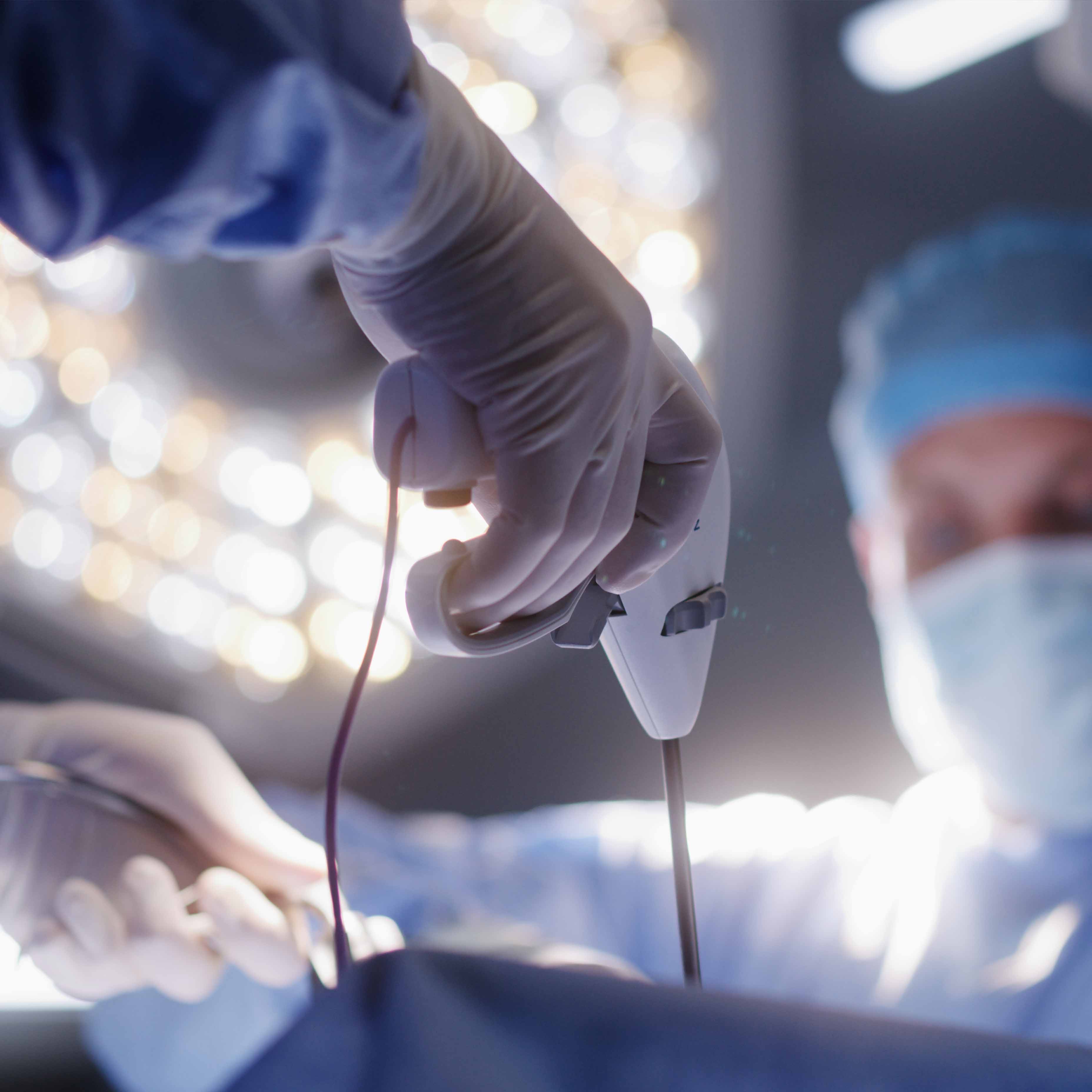 Two surgeons in an operating room. The surgeon closer to the camera is holding a small robotic device. 