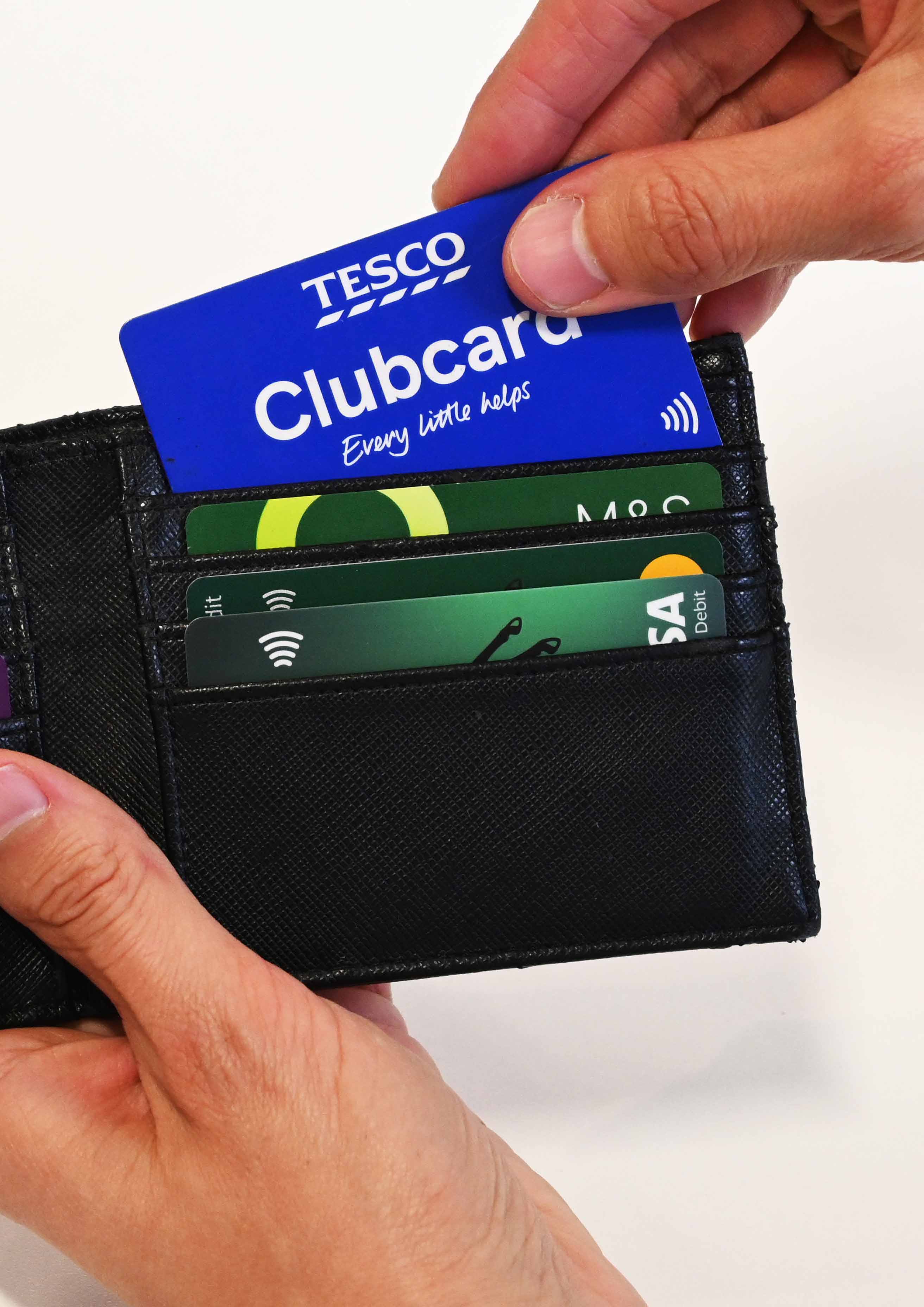 A close up of a man as he pulls out a Tesco Clubcard from a black wallet. You can see three other debit cards. 