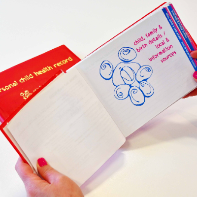 A woman is holding a personal child health record, sometimes known as the red book. It's open at a page that lists, the child family  and birth details and local and information sources.