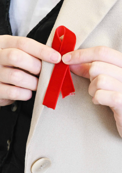 A woman is pinning a red ribbon in a cross formation to the lapel of her jacket. The pin is to show support for HIV charities.