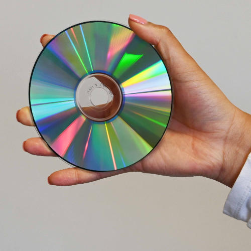 A woman holds a CD in the palm of her hand close up to the camera so you can see the rainbow holographic lights of the CD shine.