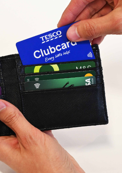 A close up of a man as he pulls out a Tesco Clubcard from a black wallet. You can see three other debit cards.