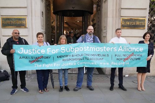 Five people stand outside Aldwych House. They look stern and serious. They're holding a turquoise banner that reads “Justice for Sub-Postmasters Alliance”. Underneath the heading there are three demands. Firstly, a full statutory inquiry, secondly a demand to identify and hold the individuals responsible to account and finally to fully recompensate the victims.