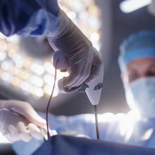 Two surgeons in an operating room. The surgeon closer to the camera is holding a small robotic device.