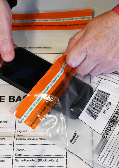 A woman puts a mobile phone into an evidence bag.