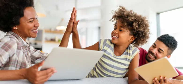 A woman holding a laptop and giving a child a high five 