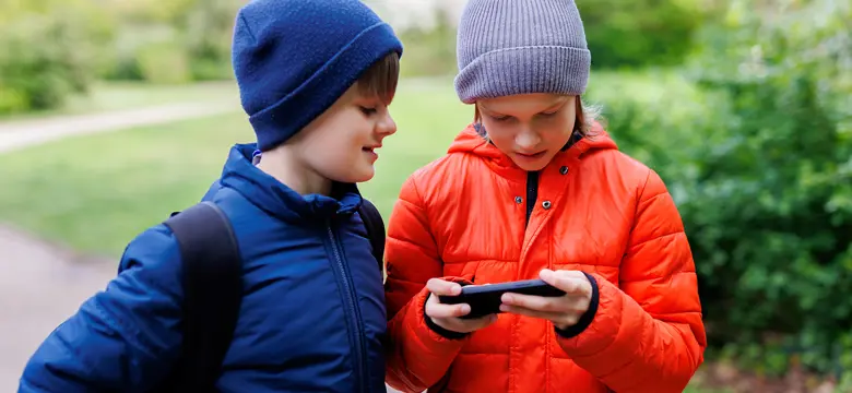 Two young children stood outside looking at a mobile phone
