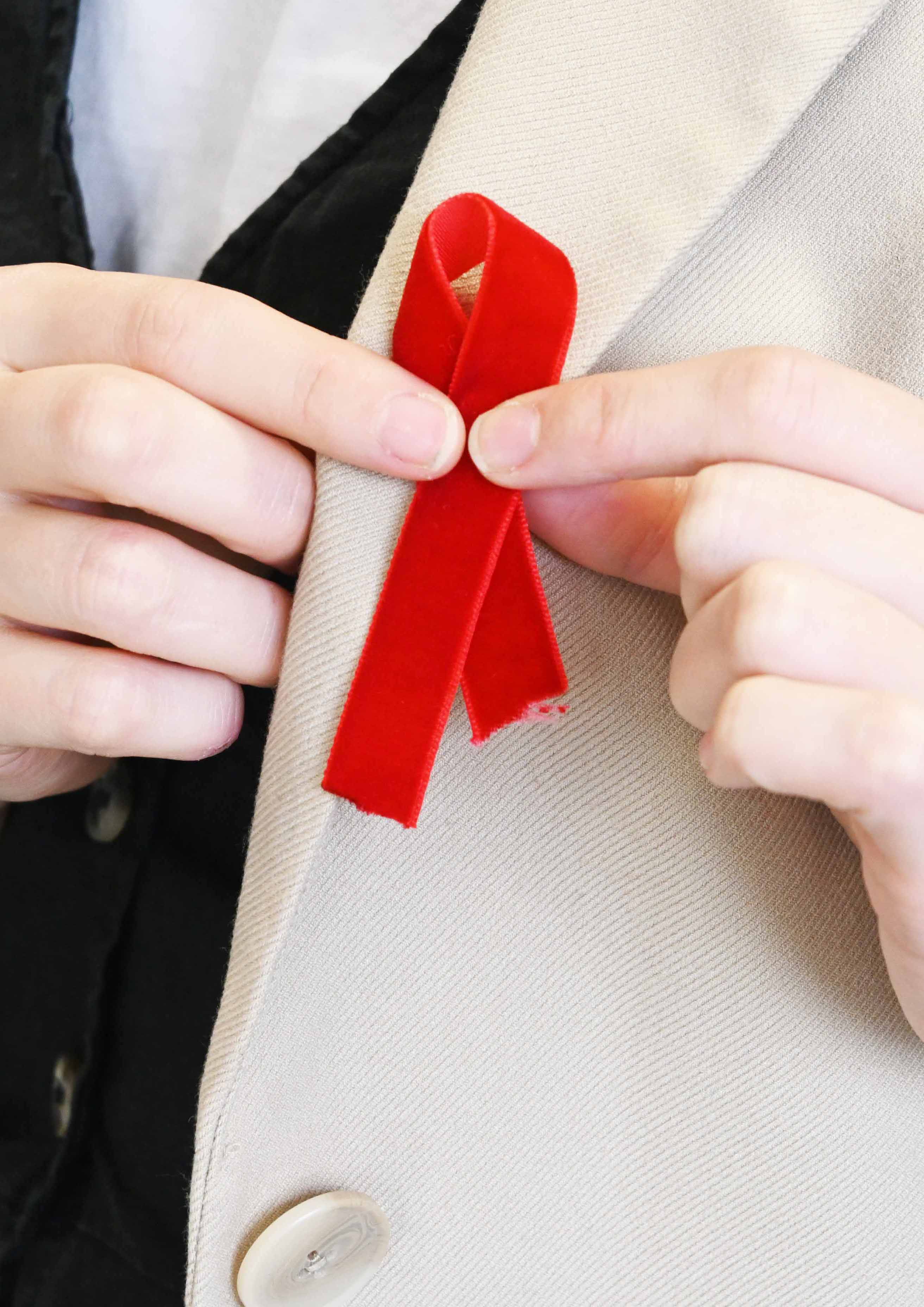 A woman is pinning a red ribbon in a cross formation to the lapel of her jacket. The pin is to show support for HIV charities.